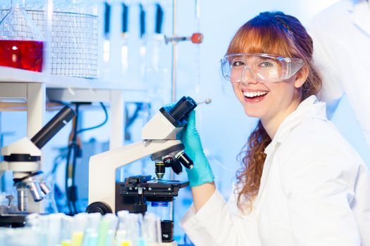 Attractive young female research scientist having fun while looking at the microscope slide in the life science laboratory. Not taking yourself to serious.