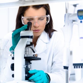 Attractive young PhD student scientist looking at the microscope slide in the life science research laboratory. Biochemistry, genetics, forensics, microbiology ..