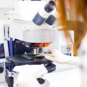 Young female scientist microscoping on hi-tec fluorescent microscope. . Health care professional in hes working environment.