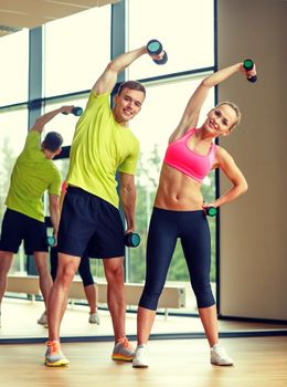 sport, fitness, lifestyle and people concept - smiling man and woman with dumbbells exercising in gym