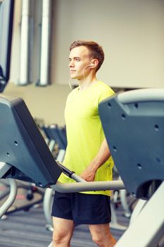 sport, fitness, lifestyle, technology and people concept - man with earphones exercising on treadmill in gym