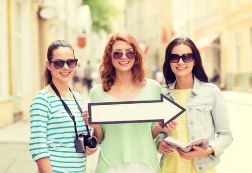 tourism, travel, vacation, direction and friendship concept - smiling teenage girls with white arrow showing direction outdoors