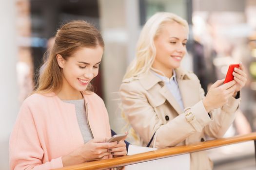 sale, consumerism, technology and people concept - happy young women with smartphones and shopping bags in mall