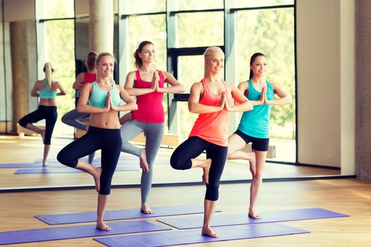 sport, meditation and lifestyle concept - smiling women meditating on mat in gym