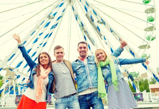 leisure, amusement park and friendship concept - group of smiling friends waving hands with ferris wheel on the back