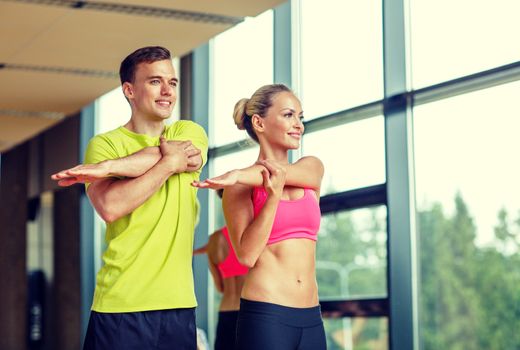 sport, fitness, lifestyle and people concept - smiling man and woman stretching in gym