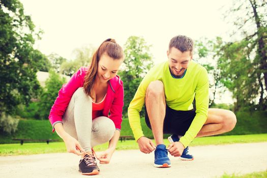fitness, sport, friendship and lifestyle concept - smiling couple tying shoelaces outdoors