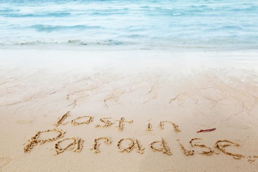 Lost in paradise concept - inscription on a beach sand with coming wave