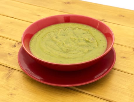 Pea and ham soup in a red bowl on a plate on a wooden table