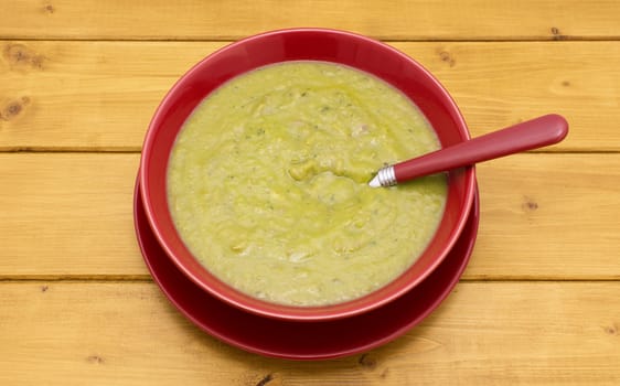 Red-handled spoon in a full bowl of green soup in a red bowl on a wooden table