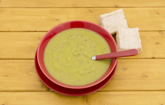 Chunks of fresh bread with bowl of green pea soup on a wooden kitchen table