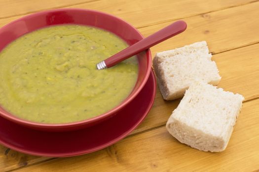 Green pea and ham soup in a red bowl, served with chunks of fresh white bread