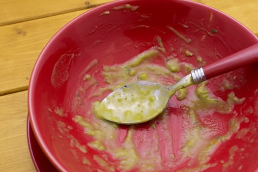Close-up of dregs of pea and ham soup in a red china bowl with a dirty spoon