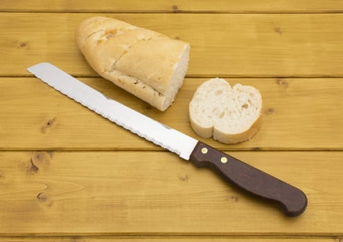 Portion of baguette with a slice cut off, bread knife beside on wooden table
