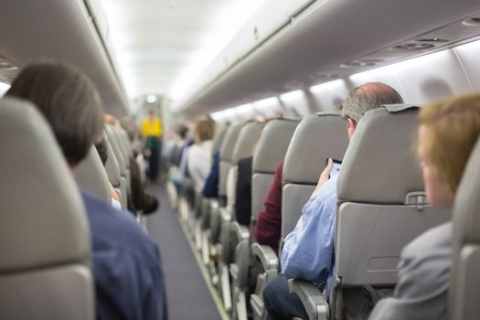 Interior of airplane with passengers on seats waiting to taik off. Stewardess in green uniform providing final safety instructions. Horizontal composition.