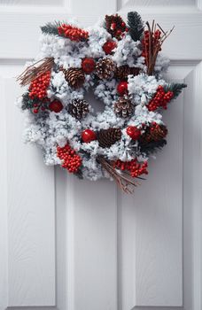 White front door decorated by Christmas wreath. Vertical photo