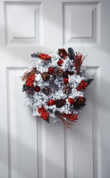White front door decorated by Christmas wreath. Vertical photo