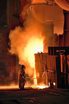 worker in a steel making factory taking sample from oven
