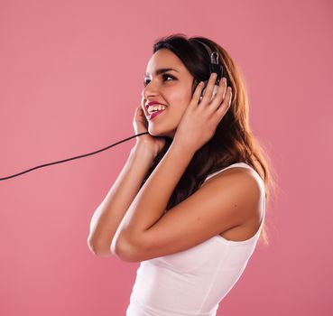 Young woman listening to music over a pink background.