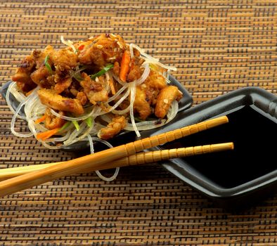 Delicious Chicken Teriyaki with Chinese Glass Noodles and Soy Sauce in Black Bowls with Chopsticks closeup on Strawmat background