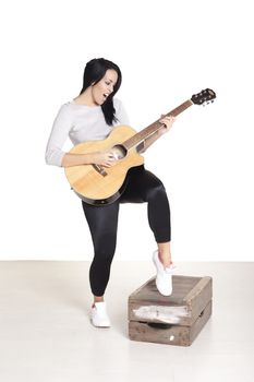 Young female busker sitting on a wooden box playing her guitar for money.