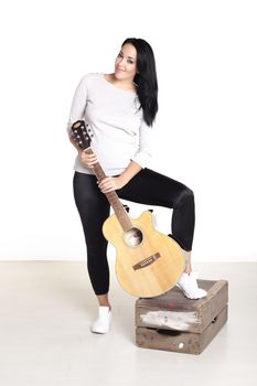 Young female busker sitting on a wooden box playing her guitar for money.