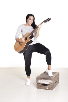 Young female busker sitting on a wooden box playing her guitar for money.