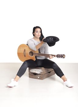 Young female busker sitting on a wooden box playing her guitar for money.