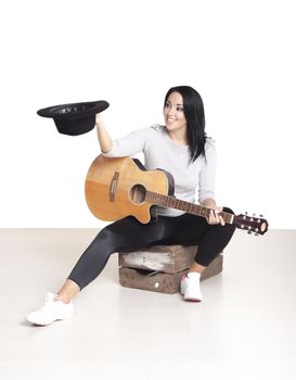 Young female busker sitting on a wooden box playing her guitar for money.
