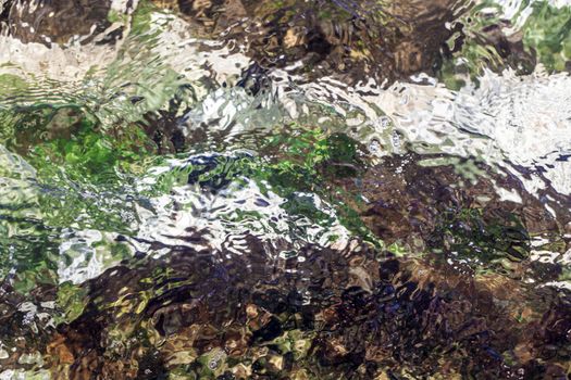 Water flowing over different coloured rocks as a abstract water background.