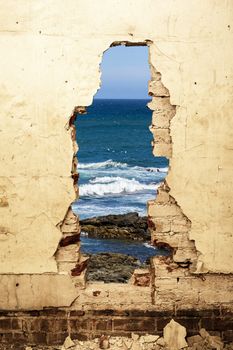 Dilapidated ocean view trough a hole in a old wall.