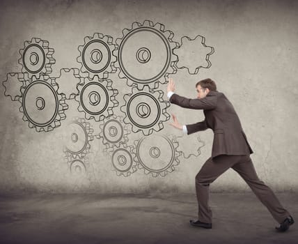 Businessman pushing cog wheel on abstract background