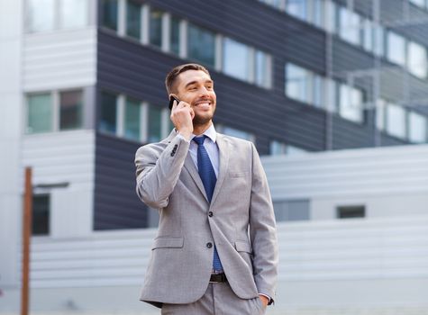 business, technology and people concept - smiling businessman with smartphone talking over office building