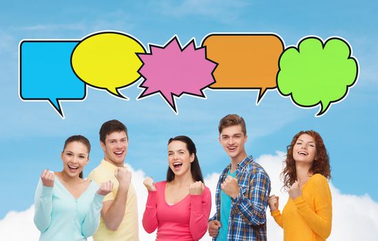 friendship, communication and people concept - group of smiling teenagers showing triumph gesture over blue sky and cloud background with text bubbles