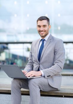 business, education, technology and people concept - smiling businessman working with laptop computer on city street