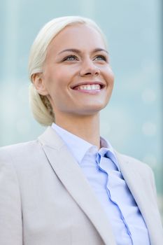 business, people and education concept - young smiling businesswoman over office building