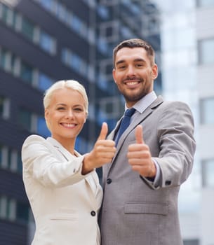 business, partnership, success, gesture and people concept - smiling businessman and businesswoman showing thumbs up over office building