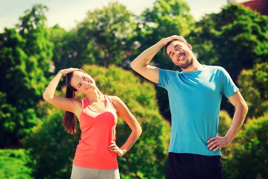 fitness, sport, training and lifestyle concept - smiling couple stretching outdoors