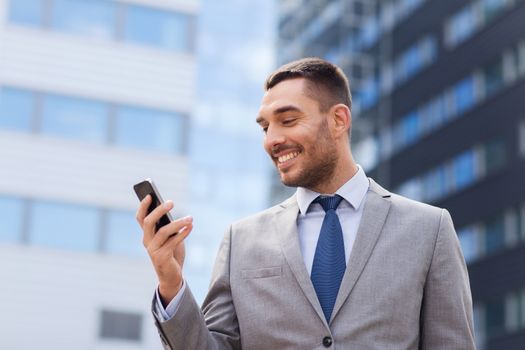 business, technology and people concept - smiling businessman with smartphone over office building