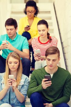 education, leisure and technology concept - busy students with smartphones sitting on staircase