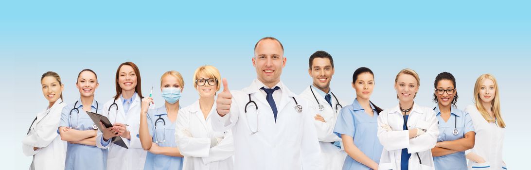 medicine, profession, teamwork and healthcare concept - international group of smiling medics or doctors with clipboard and stethoscopes with showing thumbs up over blue background