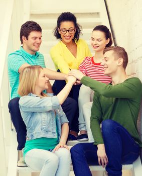 education and happiness concept - smiling students with hands on top of each other sitting on staircase