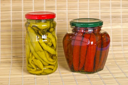 Two jars with marinated peppers on bamboo material background