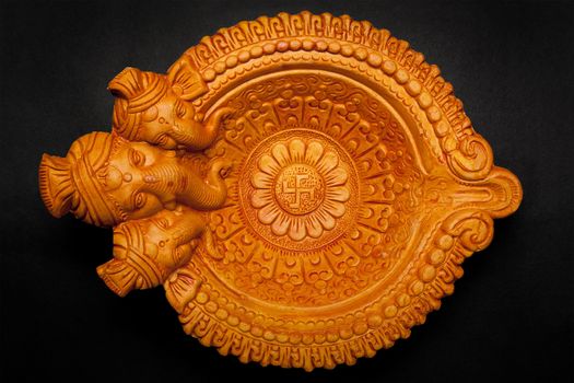 Top view of a beautifully carved designer handmade clay lamp with face of lord Ganesha isolated on dark background.