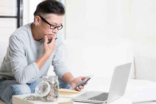 Asian mature man counting on money using calculator and laptop computer. Saving, retirement, retirees financial planning concept. Family living lifestyle at home.