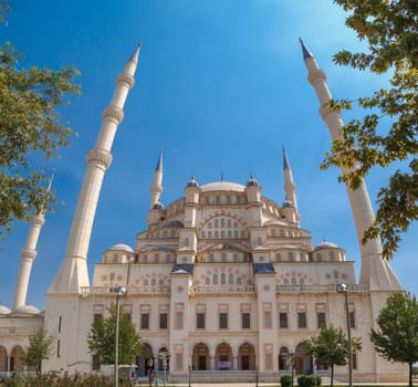 Exterior bottom view of Adana Sabanci Mosque, with six minarets, on bright blue sky background.