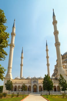 Exterior front view of Adana Sabanci Mosque, with six minarets, on bright blue sky background.