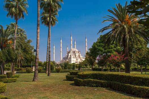 Exterior front view of Adana Sabanci Mosque, with six minarets, on bright blue sky background.