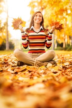 Cute young woman enjoying in sunny forest in autumn colors. She is holding golden yellow leaves. 