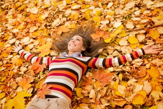 Beautiful young woman in sunny forest in autumn colors. She is lying on the fall meadow and enjoying.
